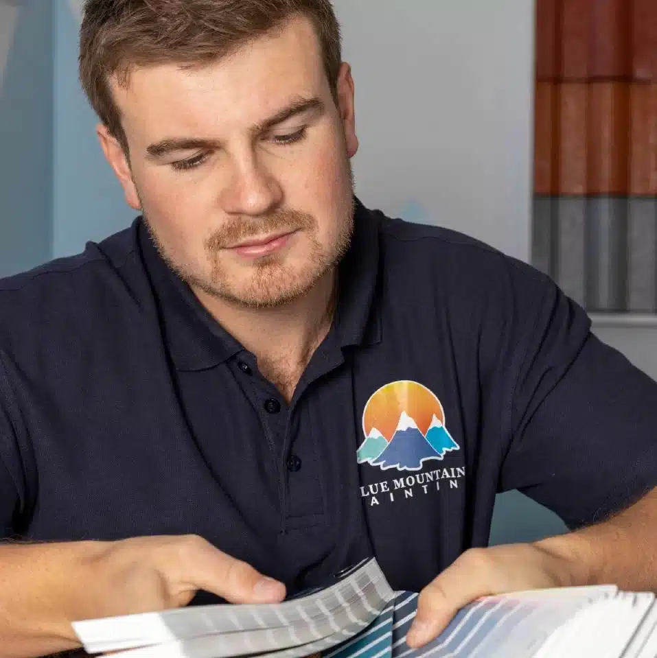 A man in a Blue Mountain Painting shirt reviews a color swatch book at a table.