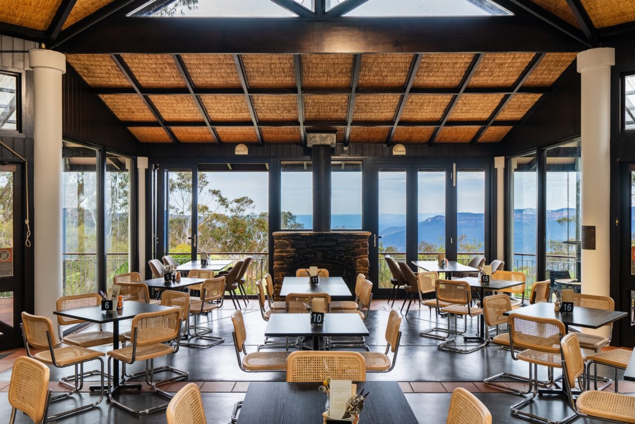 Spacious dining area with large windows, wooden ceiling, wicker chairs, and a view of mountains
