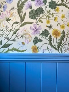 Wallpaper with botanical illustrations of various flowers and leaves above a blue wainscoting panel.