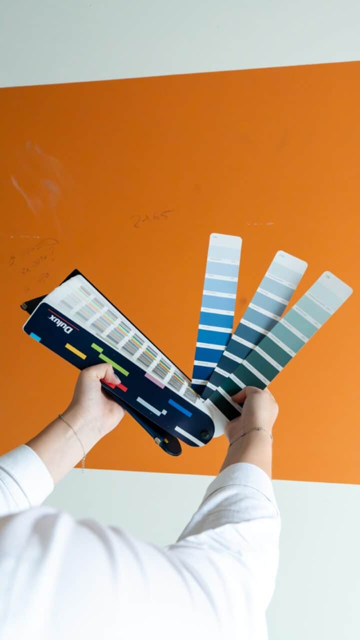 Person holding a paint color fan deck in front of an orange wall.