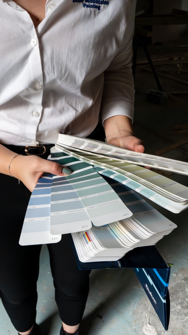 Person holding and flipping through a set of paint color swatches in an indoor setting.