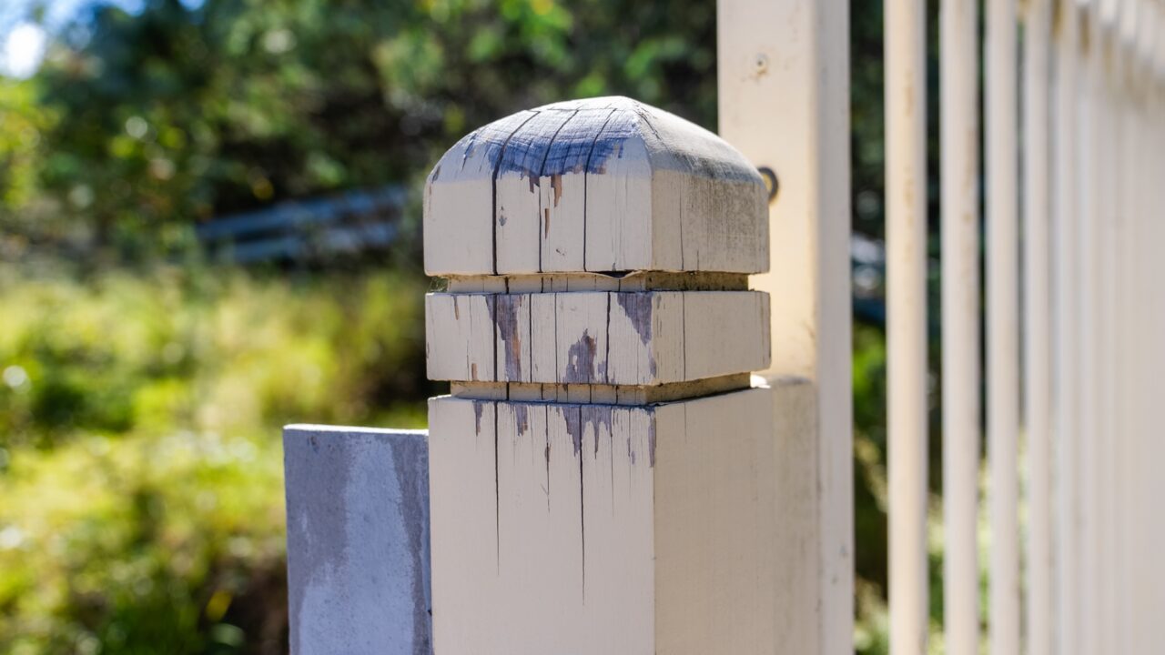Close-up of a weathered wooden fence posts with peeling paint, set against a blurred background