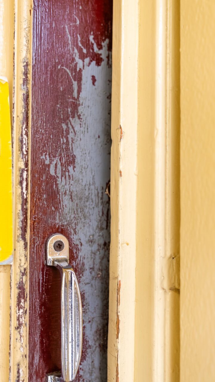 Close-up photo of an old, chipped door frame painted yellow with a metal handle