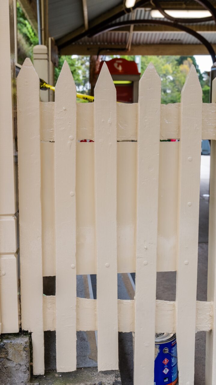 White wooden picket fence standing with a paint can and brush behind it
