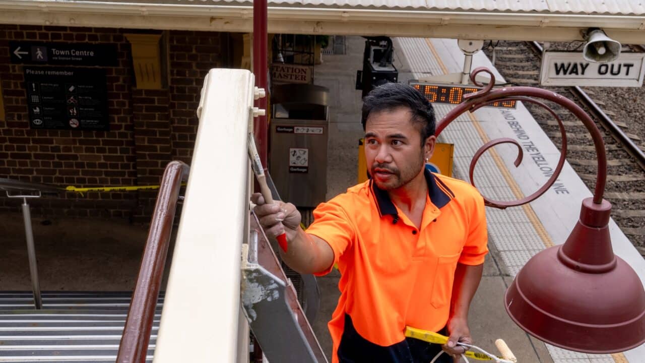 A worker in an orange high-visibility shirt painting a railing