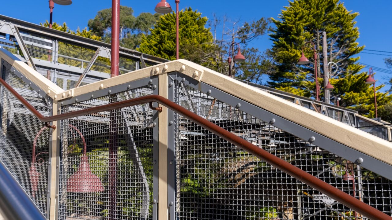 View of an outdoor staircase with metal railings and a wooden handrail surrounded by trees