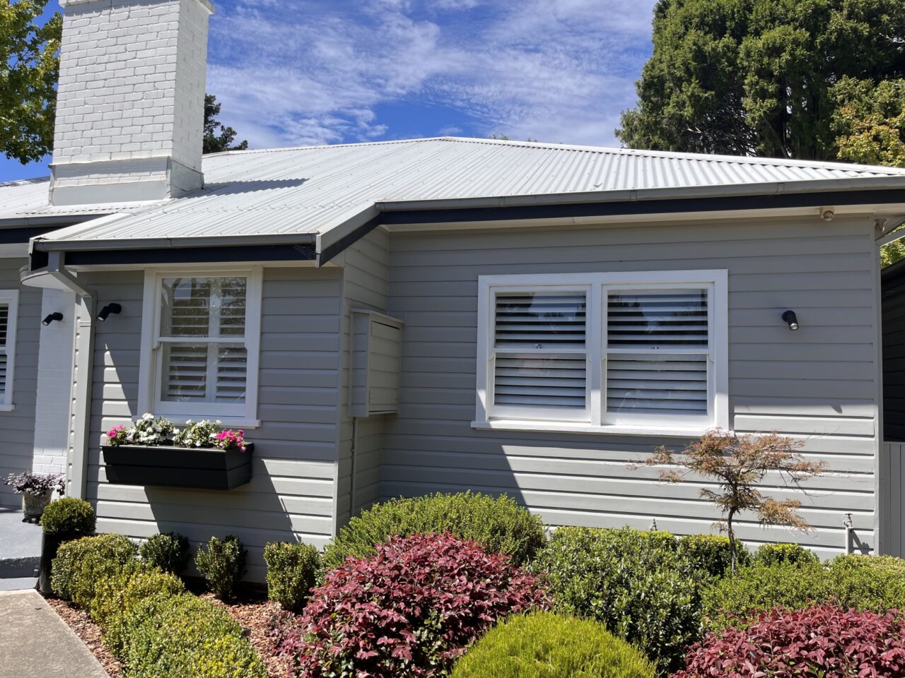A small, single-story house with light gray siding, white trim, and a metal roof