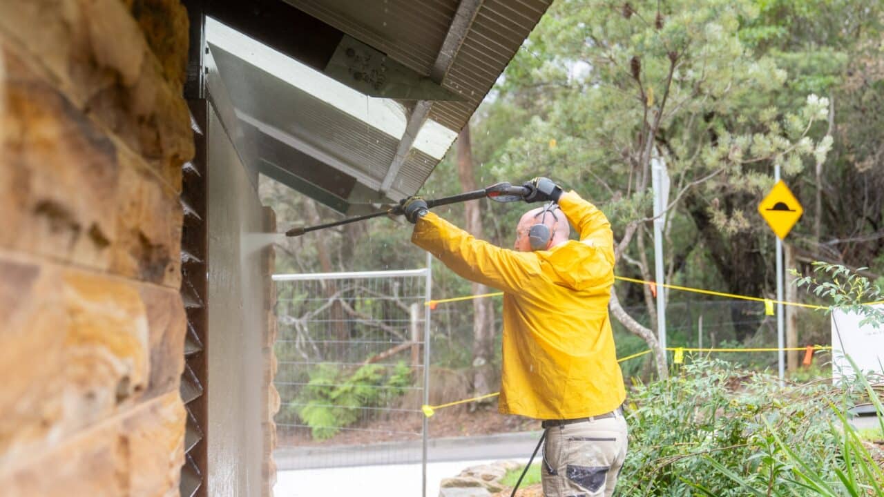 Person in a yellow jacket power washing the side of a building.