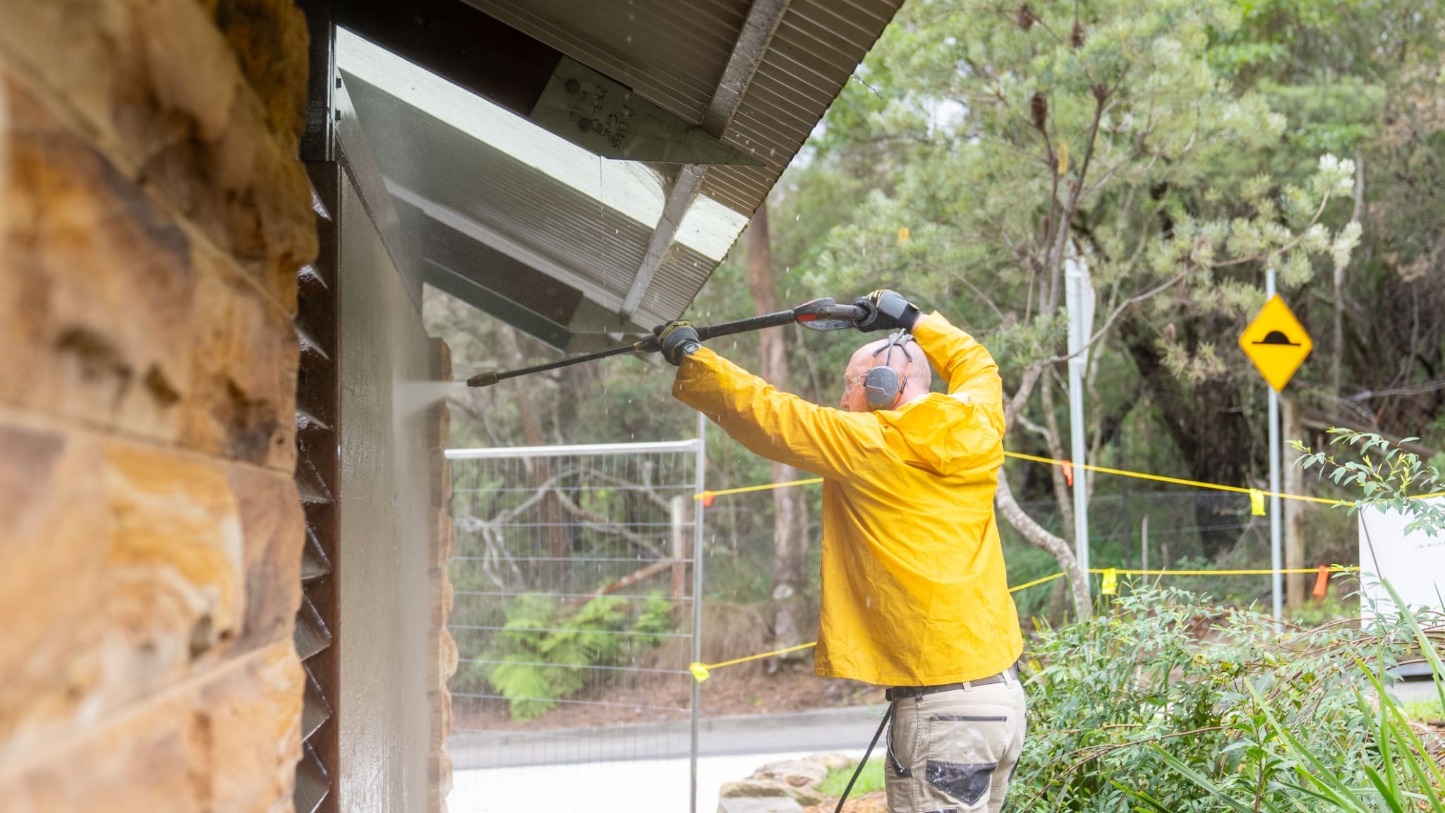 Person in a yellow jacket power washing the side of a building.