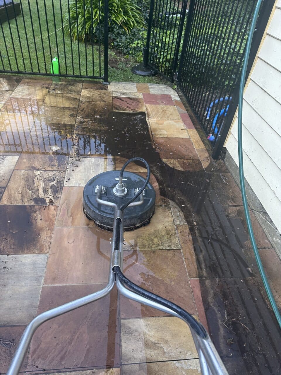 A pressure washer cleaning a stained, wet patio with stone tiles