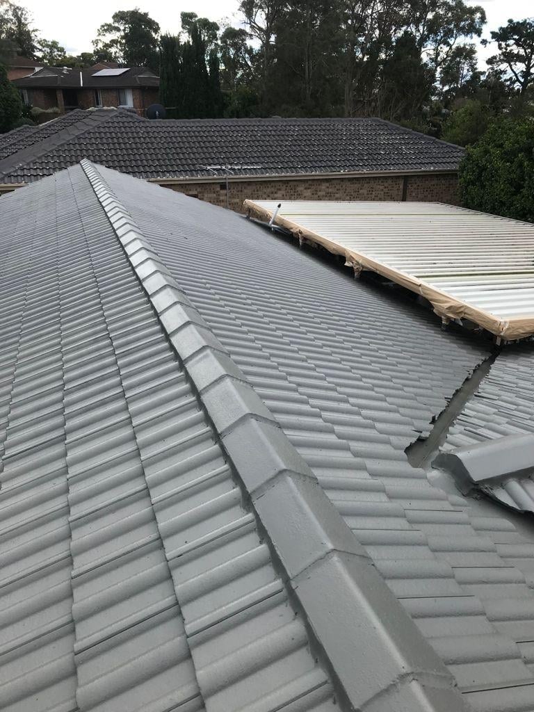 Close-up view of a grey tiled roof with overlapping tiles, some sections have missing tiles