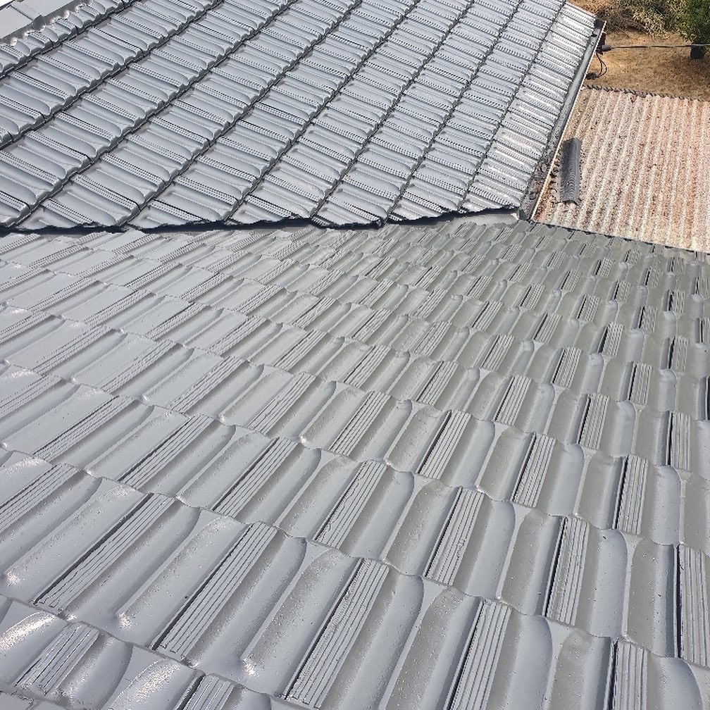 Close-up view of a roof with grey, interlocking ceramic tiles and a section of a different roofing
