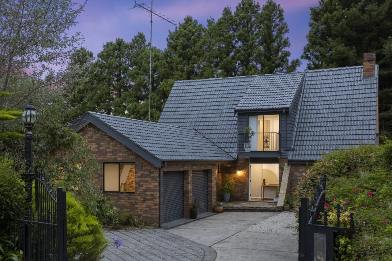 A two-story brick house with a gray tiled roof, surrounded by trees