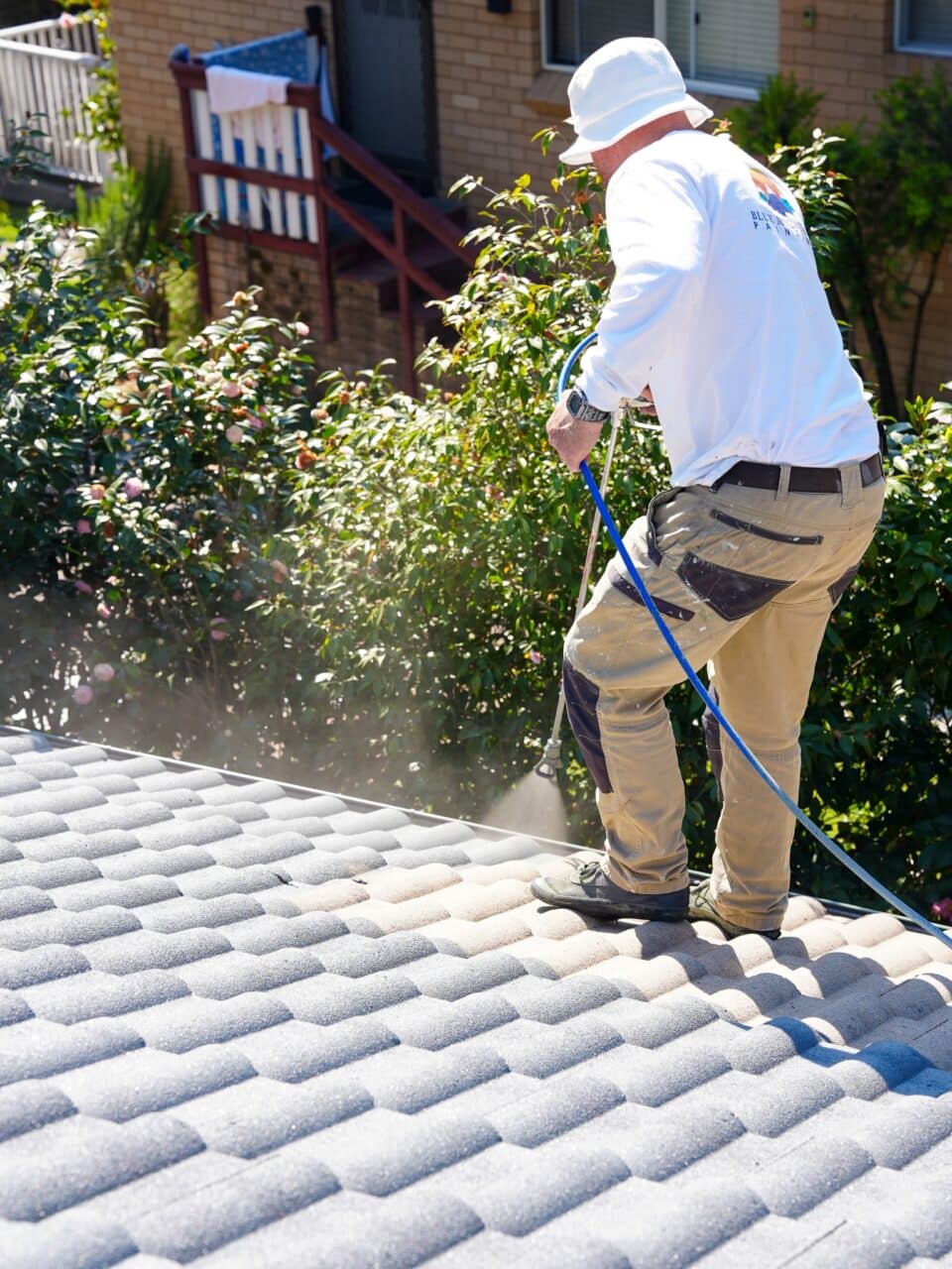 Person in work clothes and a hat using a hose to clean a tiled roof