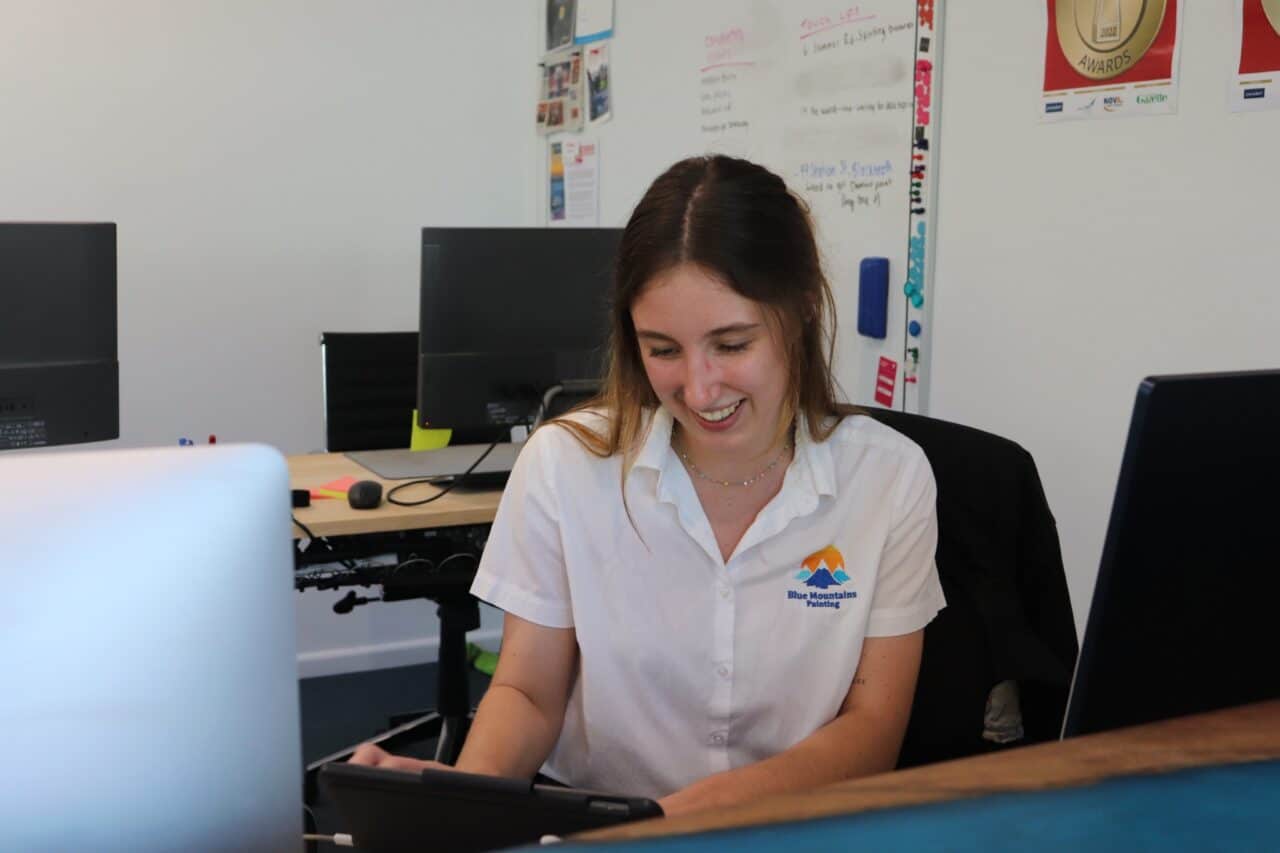 Woman in a white blouse sitting at a desk, smiling and using a tablet