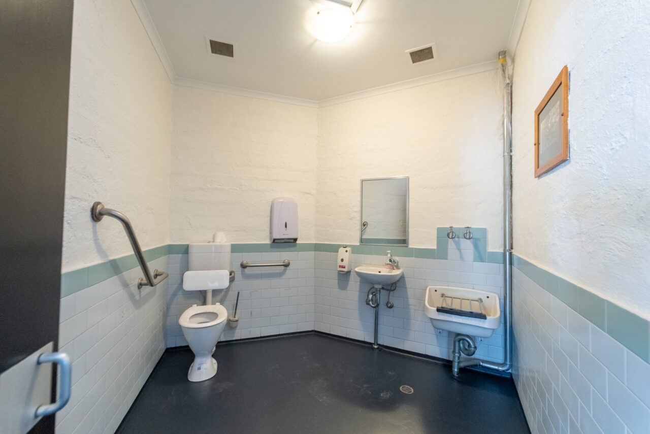 A clean, spacious public restroom with a toilet, sink, soap dispenser & wall-mounted mirror