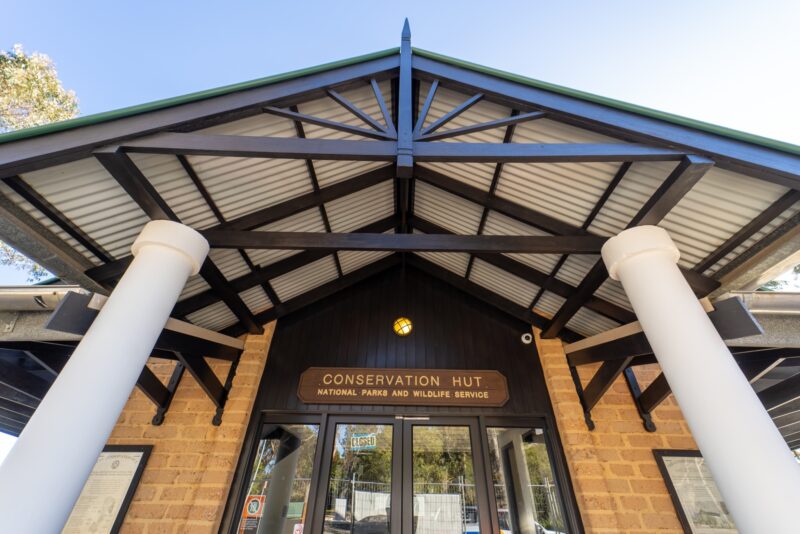 Entrance to the Conservation Hut building with large white pillars, sloped roof, and a brown sign.