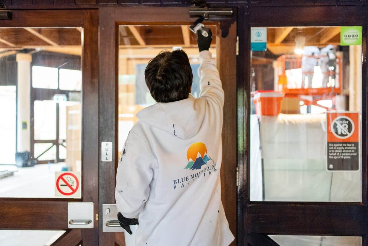 A person in a "Blue Mountain Painting" hoodie painting a wooden door.