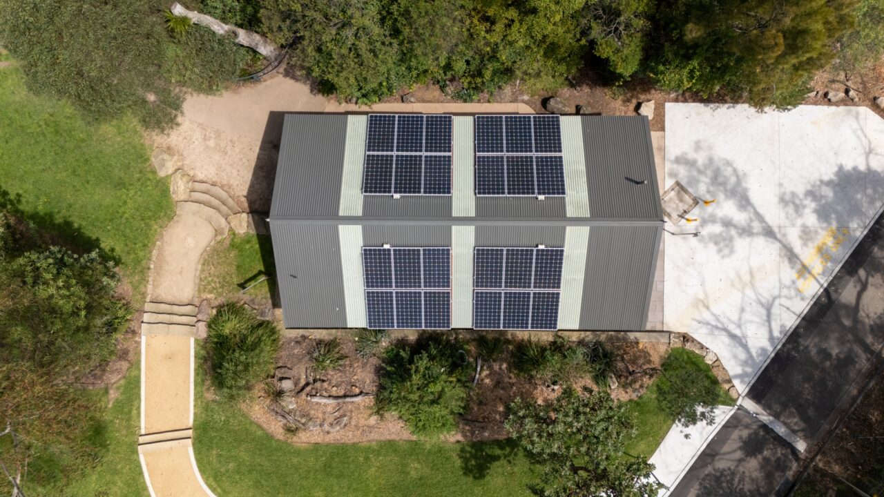 Aerial view of a building with eight solar panels on its roof, nestled amid the greenery