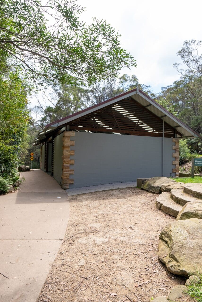 A public restroom building with a green exterior, surrounded by trees and rocks