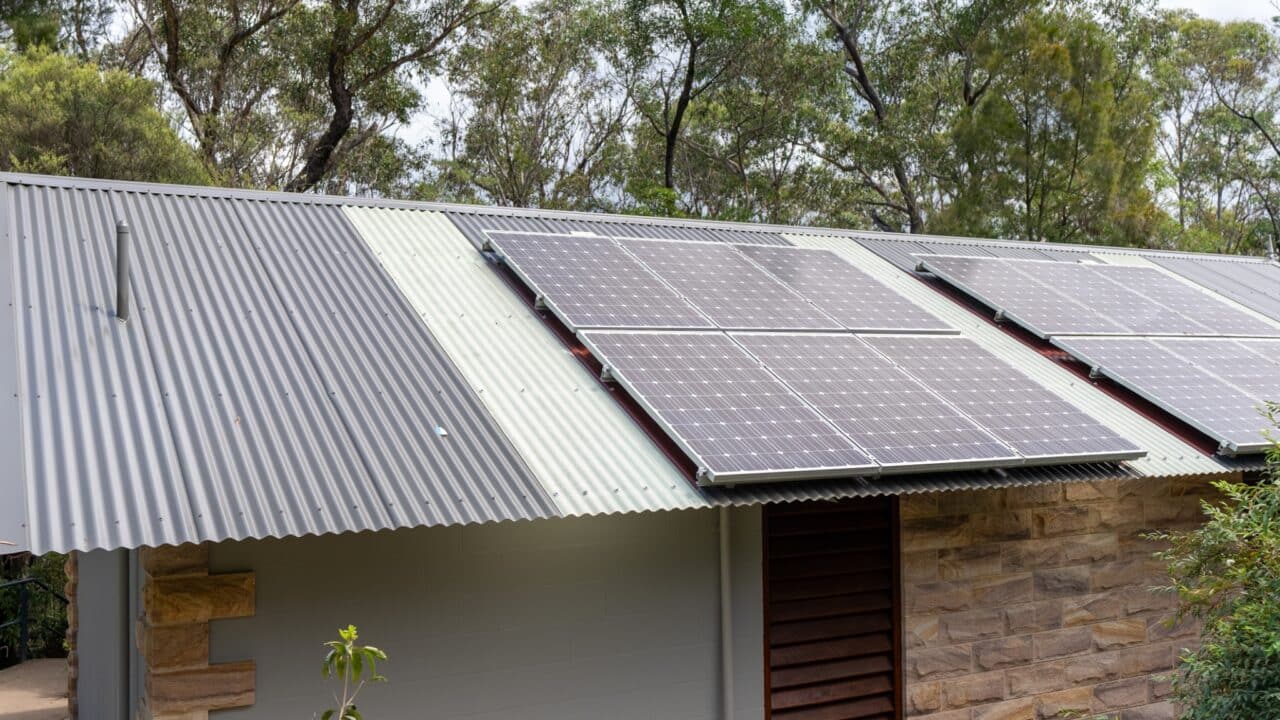 A corrugated metal roof with installed solar panels surrounded by trees