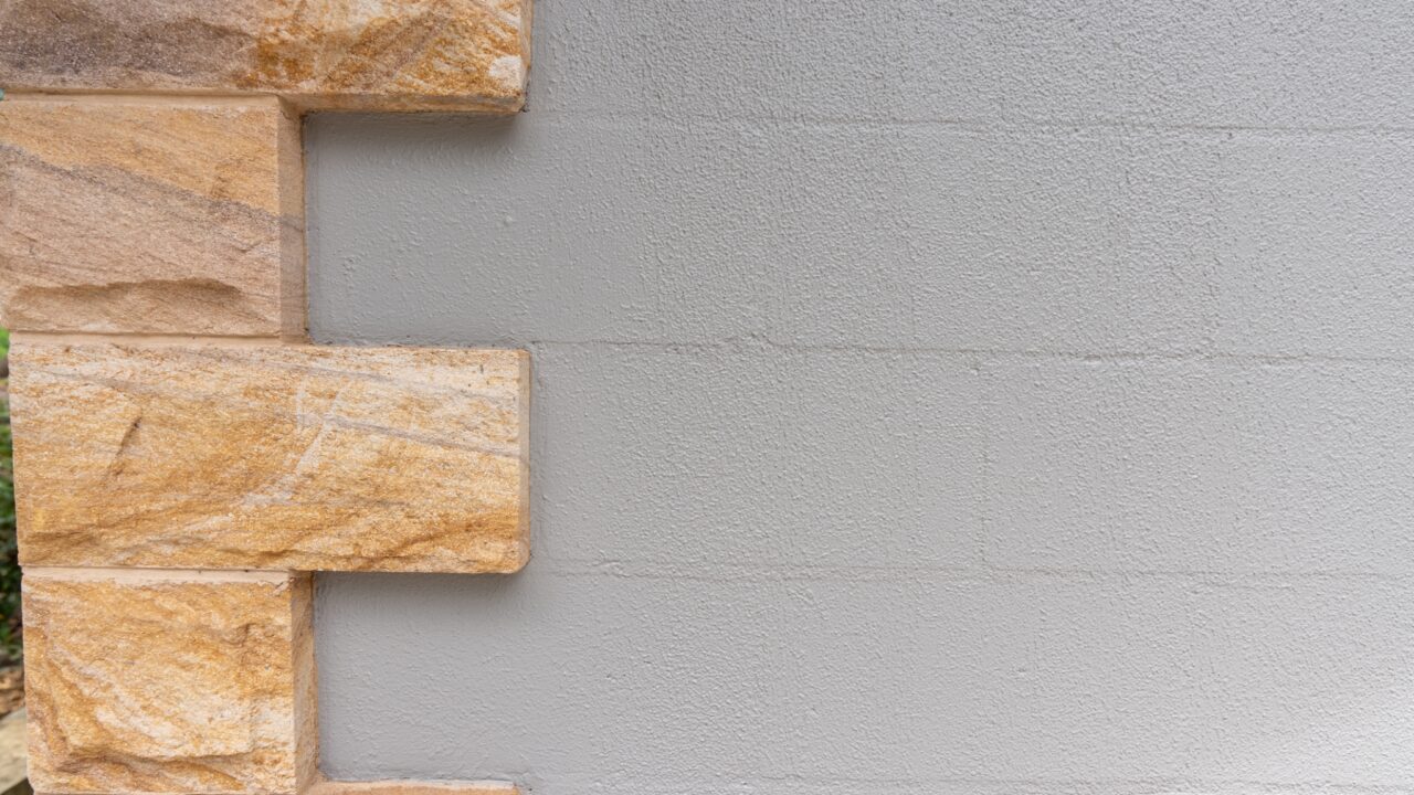 Section of wall with rectangular light brown stone bricks interlocked on the left and gray plaster