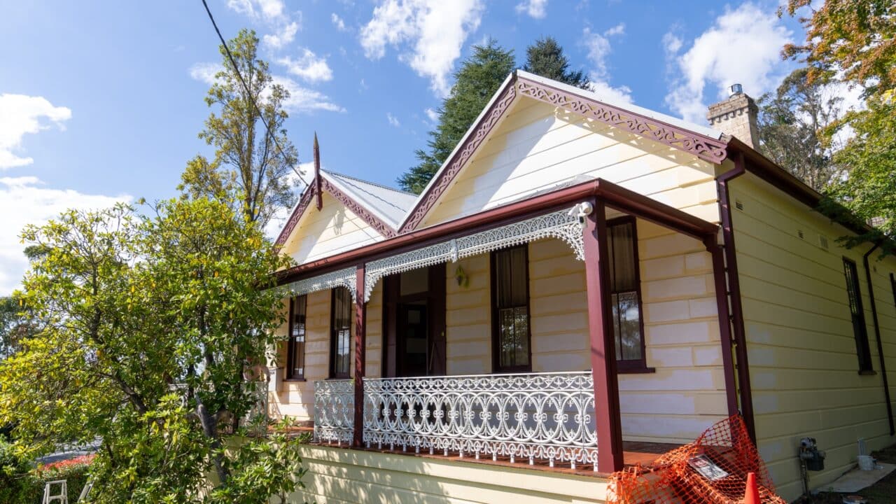 A yellow and white house with ornate red trim and a veranda featuring intricate white railing