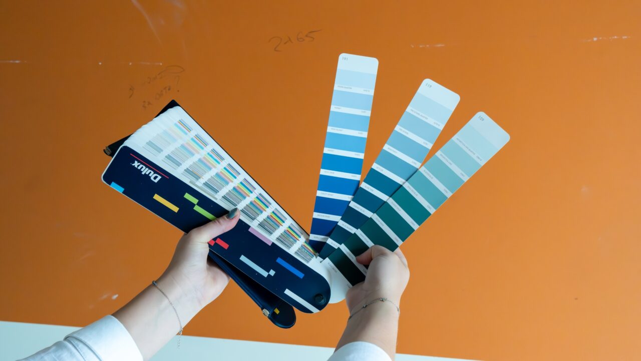 Person holding a color swatch book against an orange wall.
