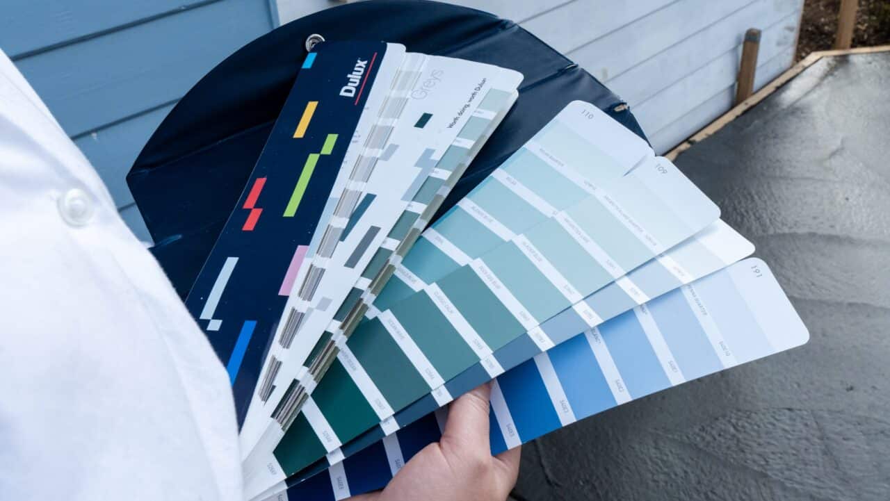 A person holding a fanned-out collection of paint color swatches, displaying a range of blue and gray shades.