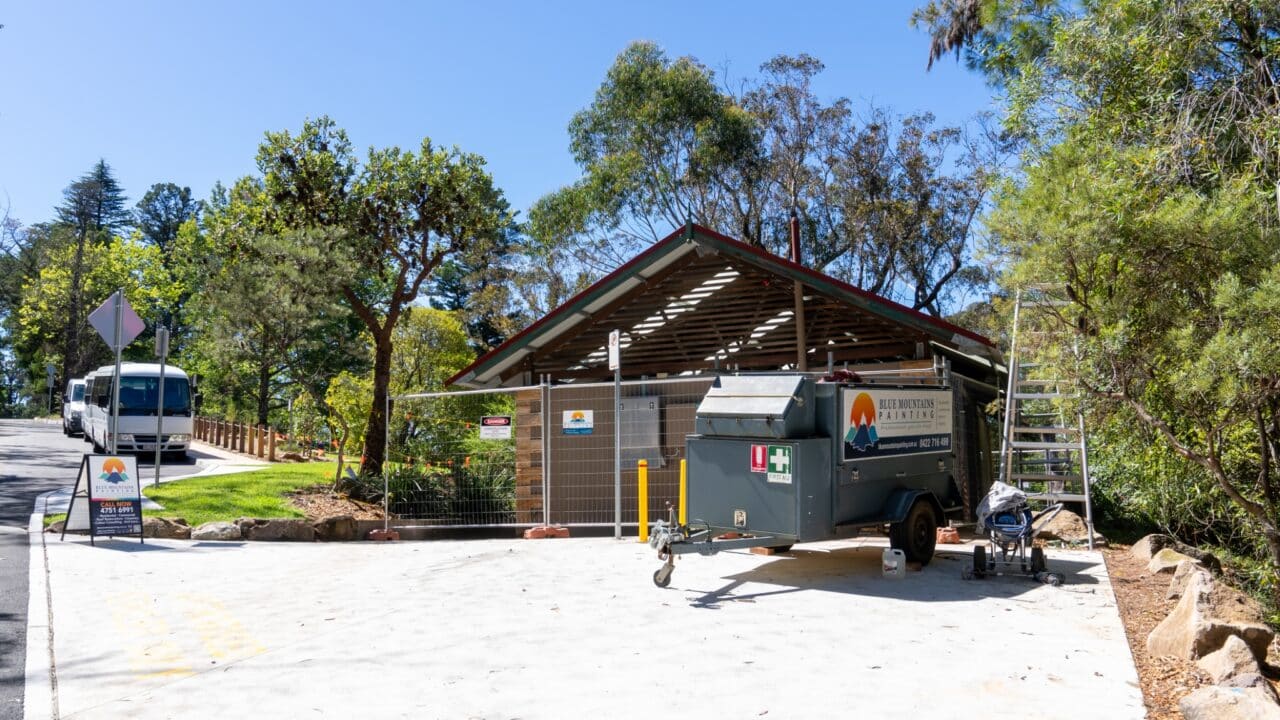 A construction site with a trailer and equipment in front of a building surrounded by trees