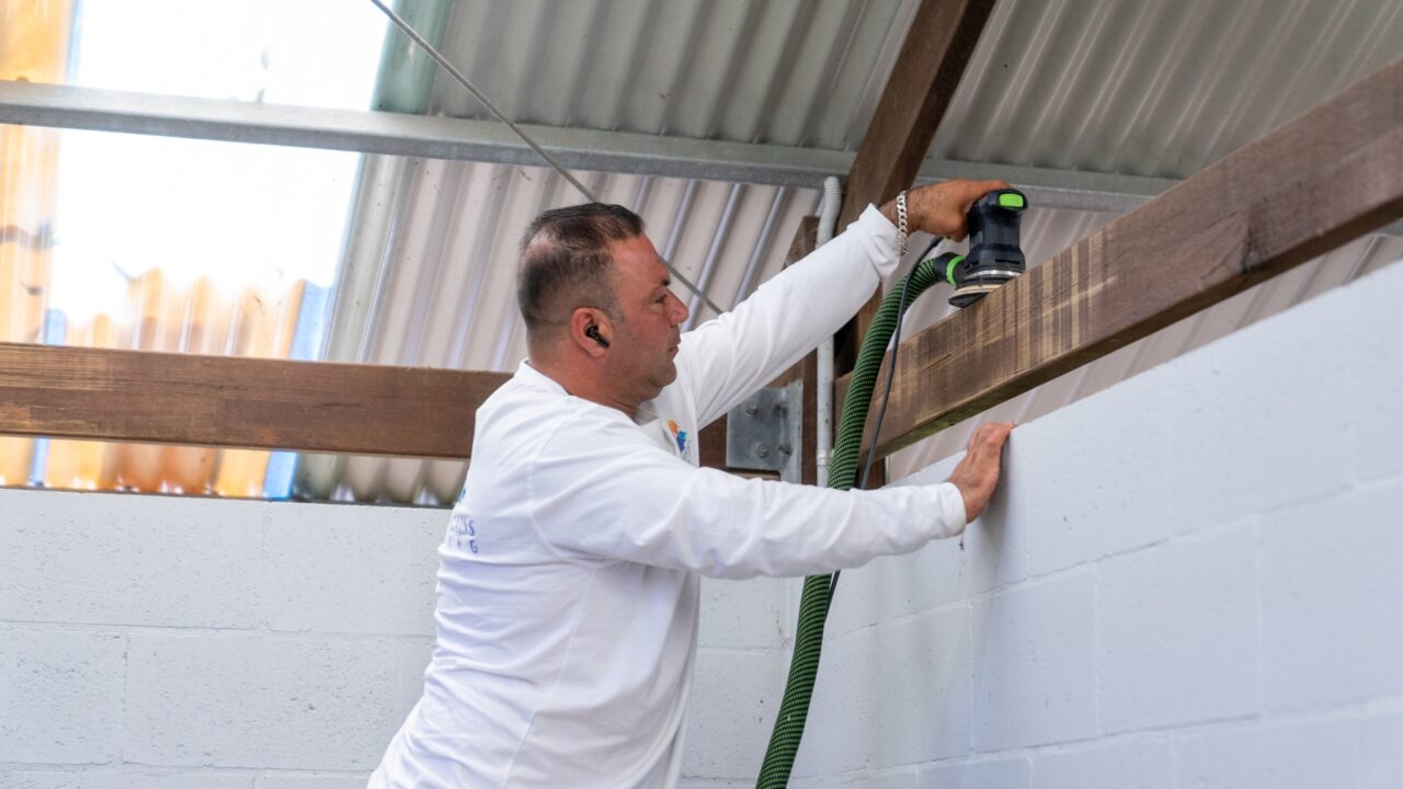 Person in a white long-sleeve shirt sanding a piece of wood with a power sander