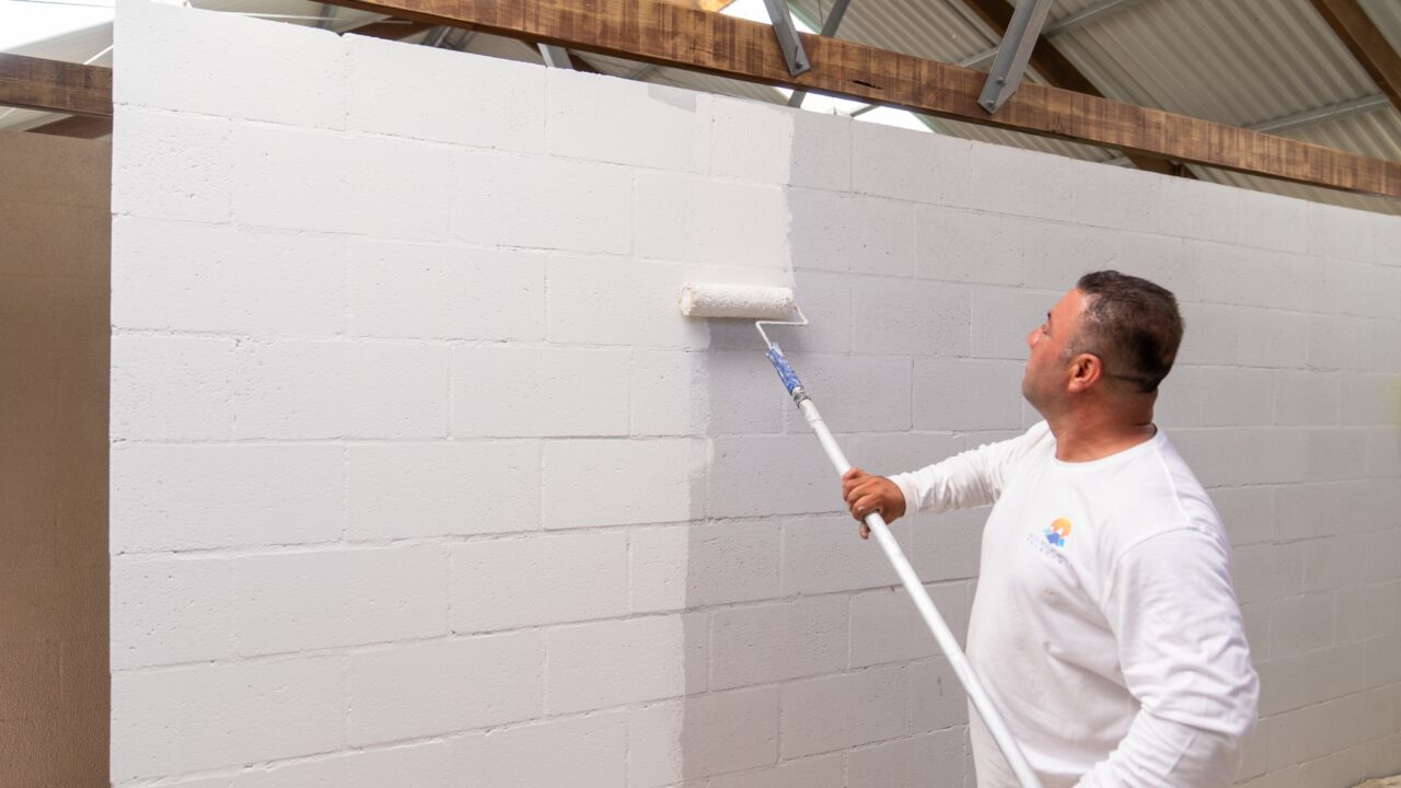 Man in white shirt transforming a cinder block wall using a long-handled roller
