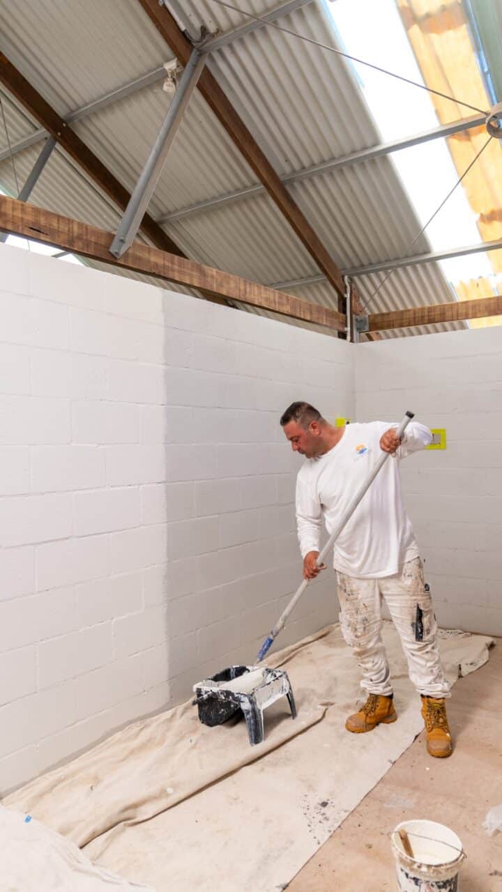 Person in white attire and brown boots painting a white wall with a roller