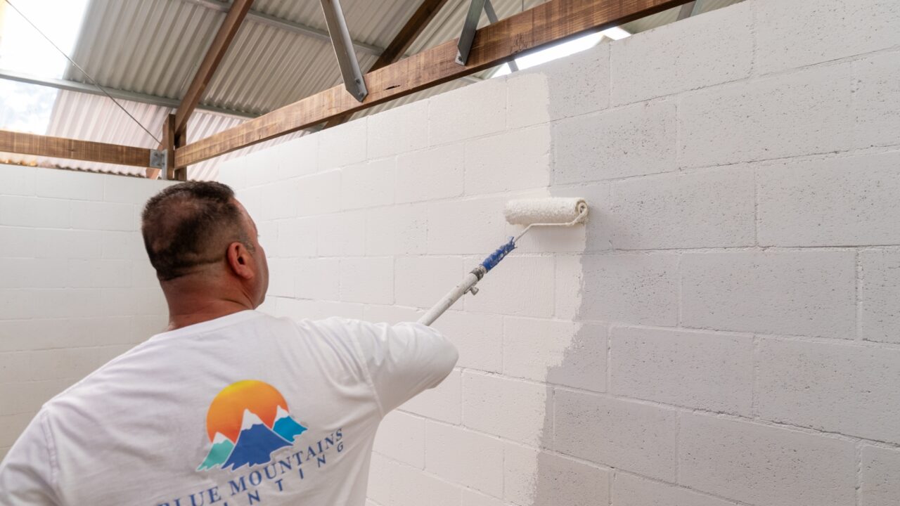 Person painting a white concrete wall with a roller attached to an extension pole
