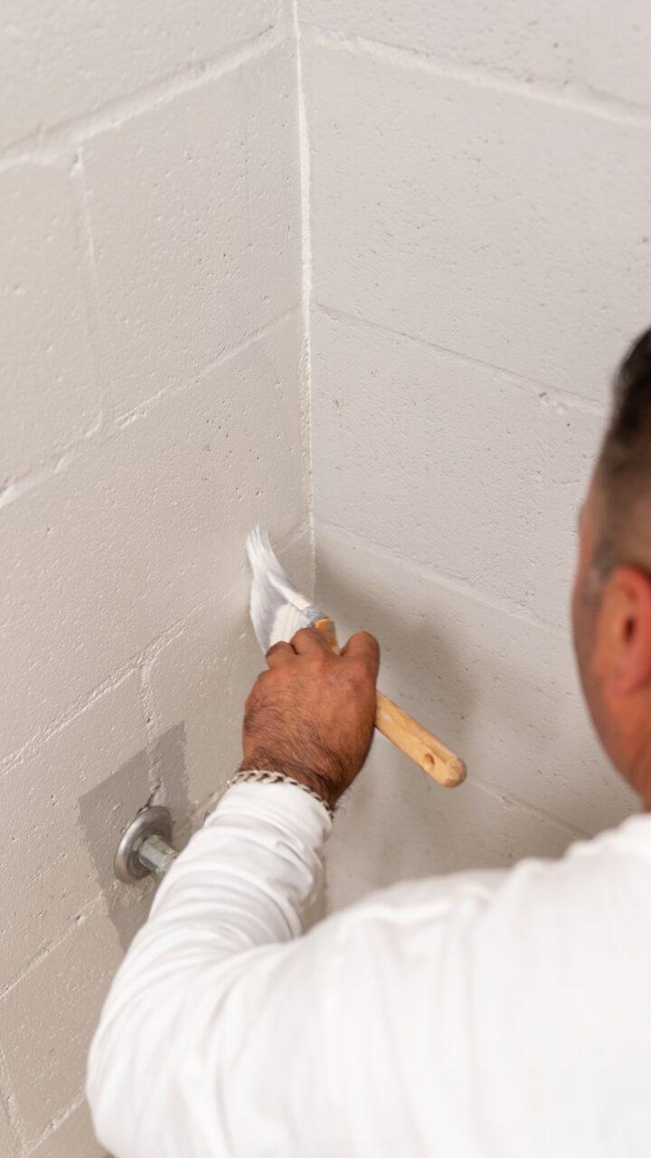 A person painting a white wall in the corner of a room with a paintbrush