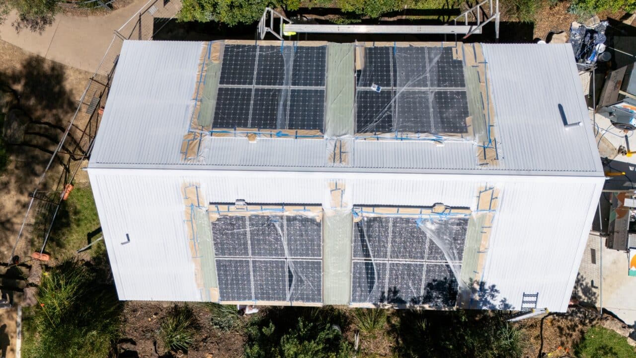 Aerial view of a white building with solar panels on its roof, surrounded by greenery