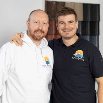 Two men standing together indoors, smiling at the camera.