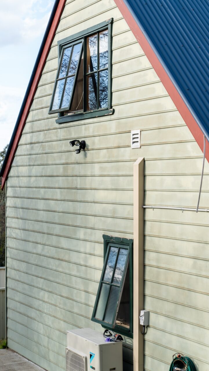 The bullaburra house features a light green wooden exterior with a blue metal roof.