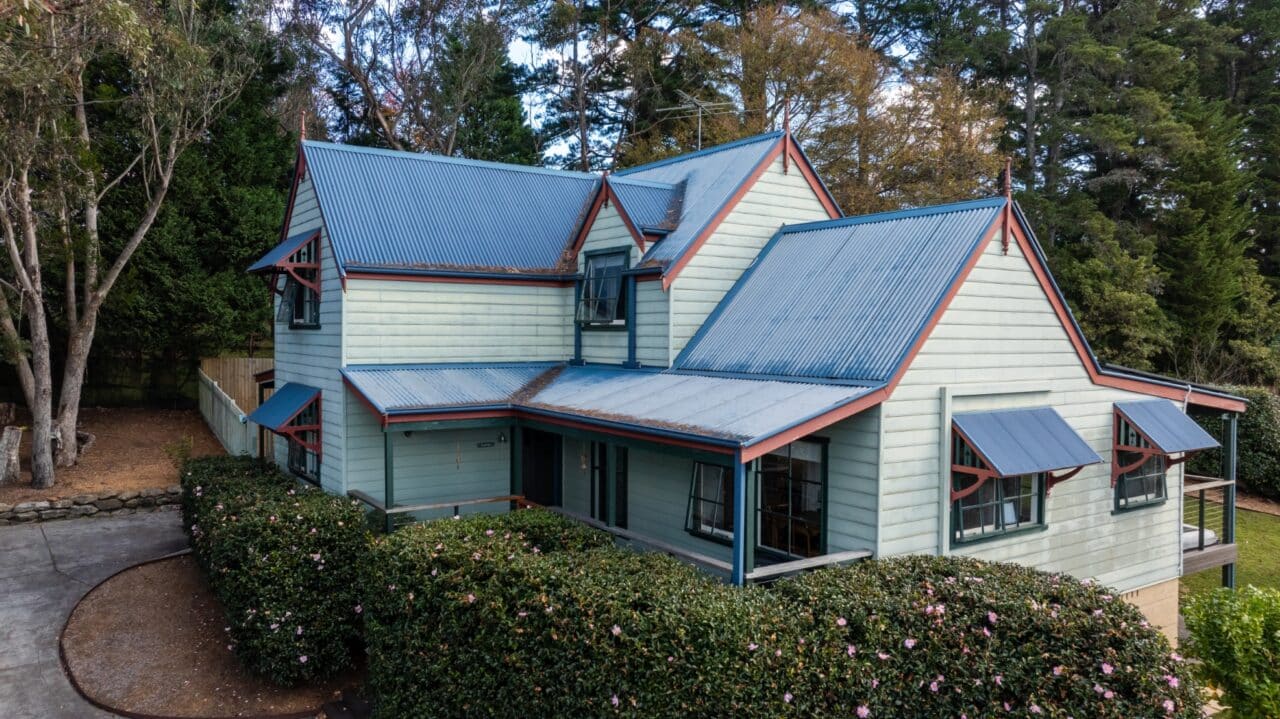 Charming two story bullaburra house with light green siding and a blue metal roof.