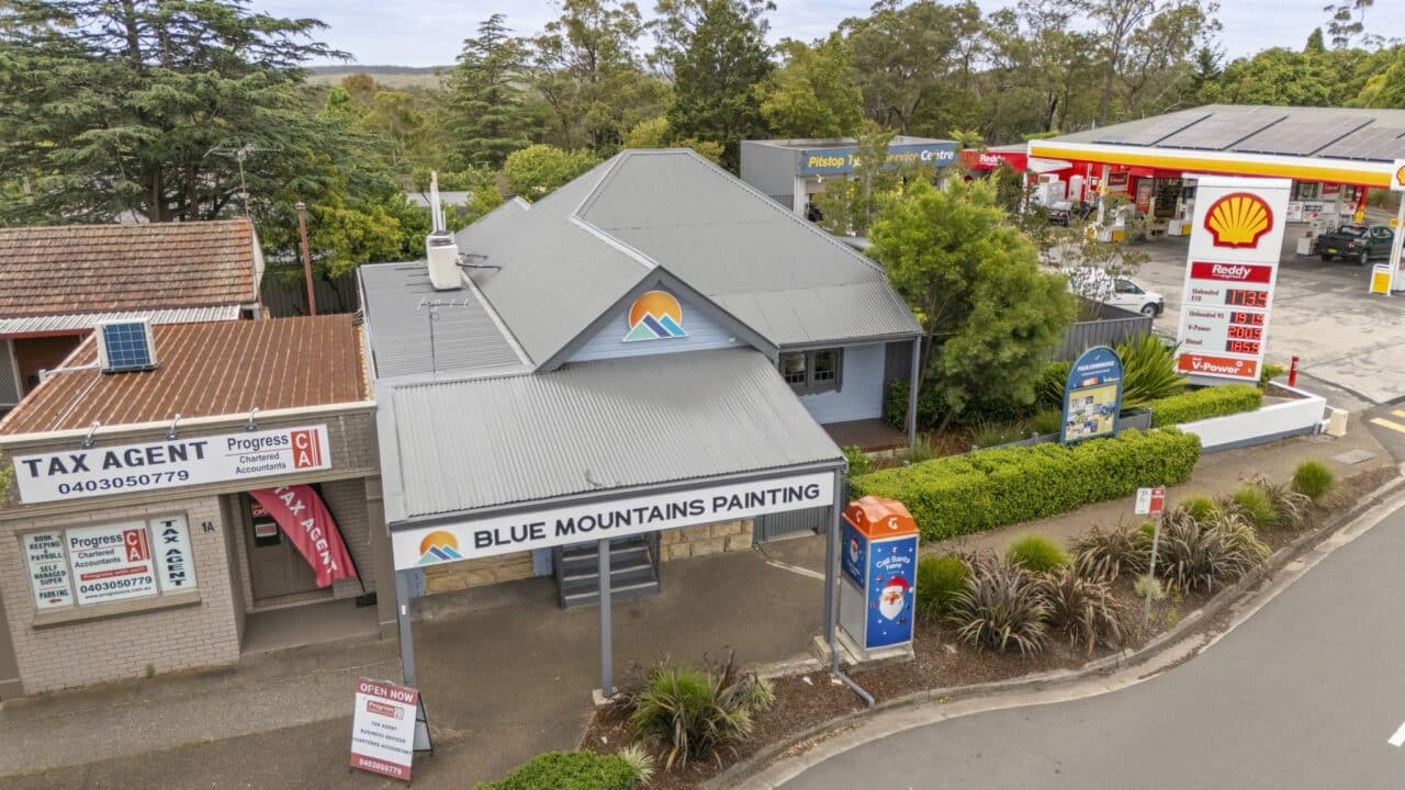 small building with blue mountains painting stands adjacent to a tax agent officer & gas station