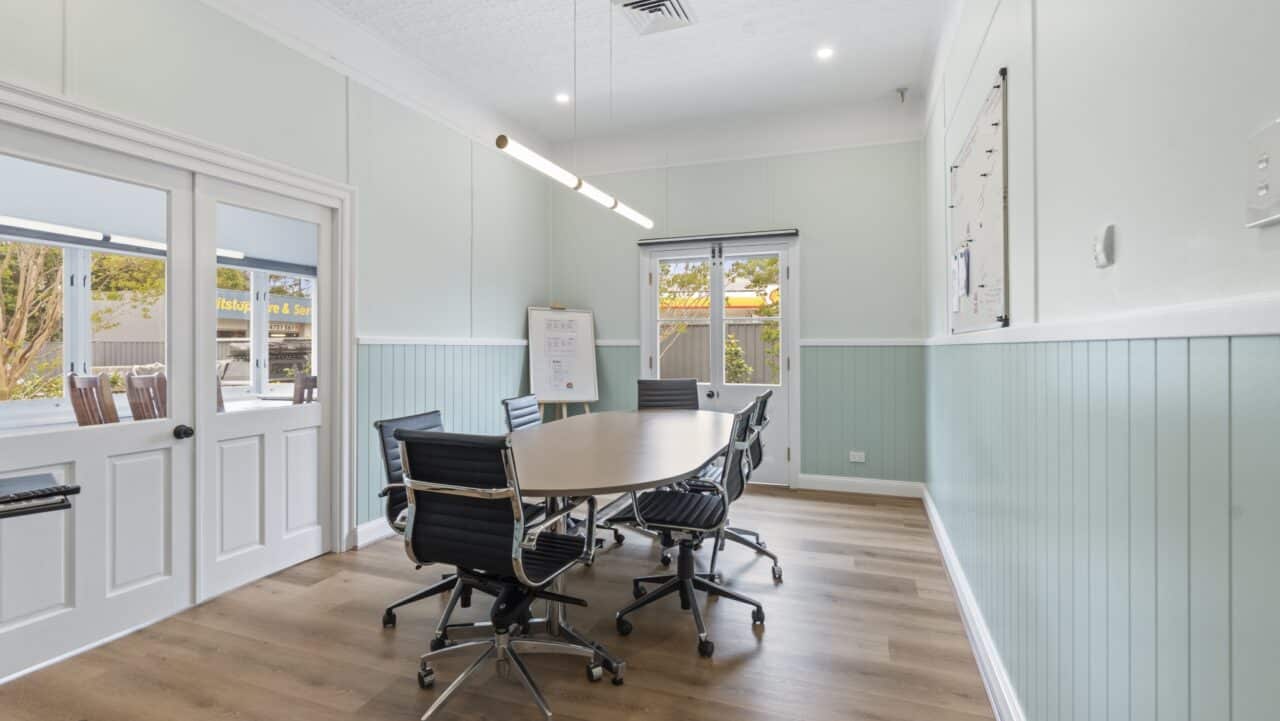 Meeting room in bullaburra with a long oval table, black chairs, and a wall mounted whiteboard.