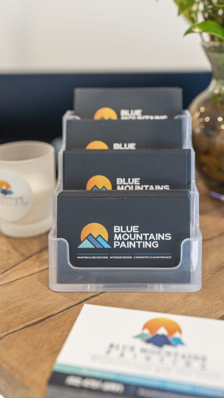 business cards for "blue mountains painting" in a clear holder on a wooden table