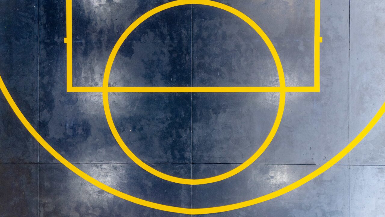 aerial view of the basketball court at springwood high school, showcasing bright yellow line marking on a dark gray surface, featuring part of the center circle and three point line.