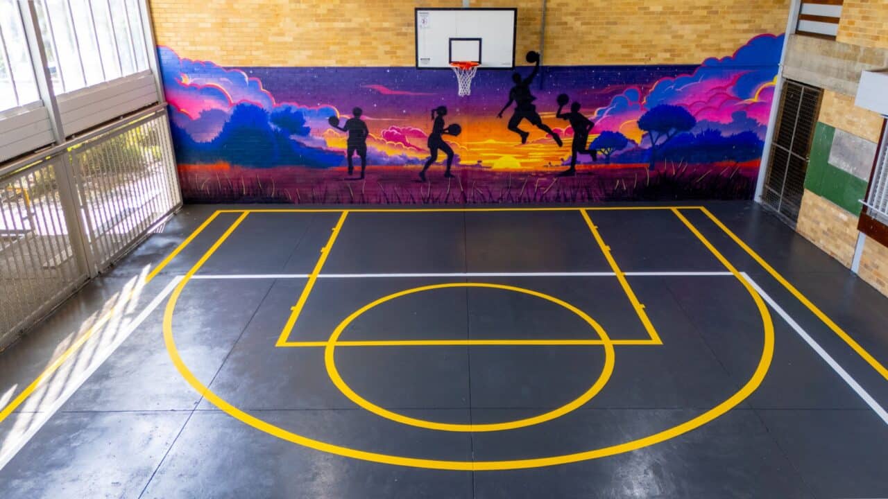 the indoor basketball court at springwood high school features a mural of silhouetted figures playing against a vibrant sunset background, with precise line markings enhancing the overall aesthetic.