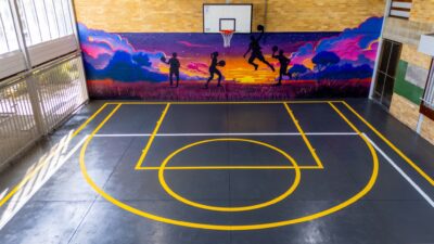 the indoor basketball court at springwood high school features a mural of silhouetted figures playing against a vibrant sunset background, with precise line markings enhancing the overall aesthetic.