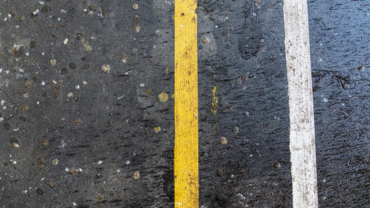 close up of a wet road near springwood high school, showcasing line marking with a yellow line beside a white one, dotted by scattered circular spots on the surface.
