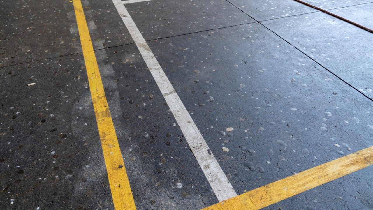 the wet concrete floor at springwood high school features intersecting yellow and white lines with visible water spots, highlighting the precision of line marking.