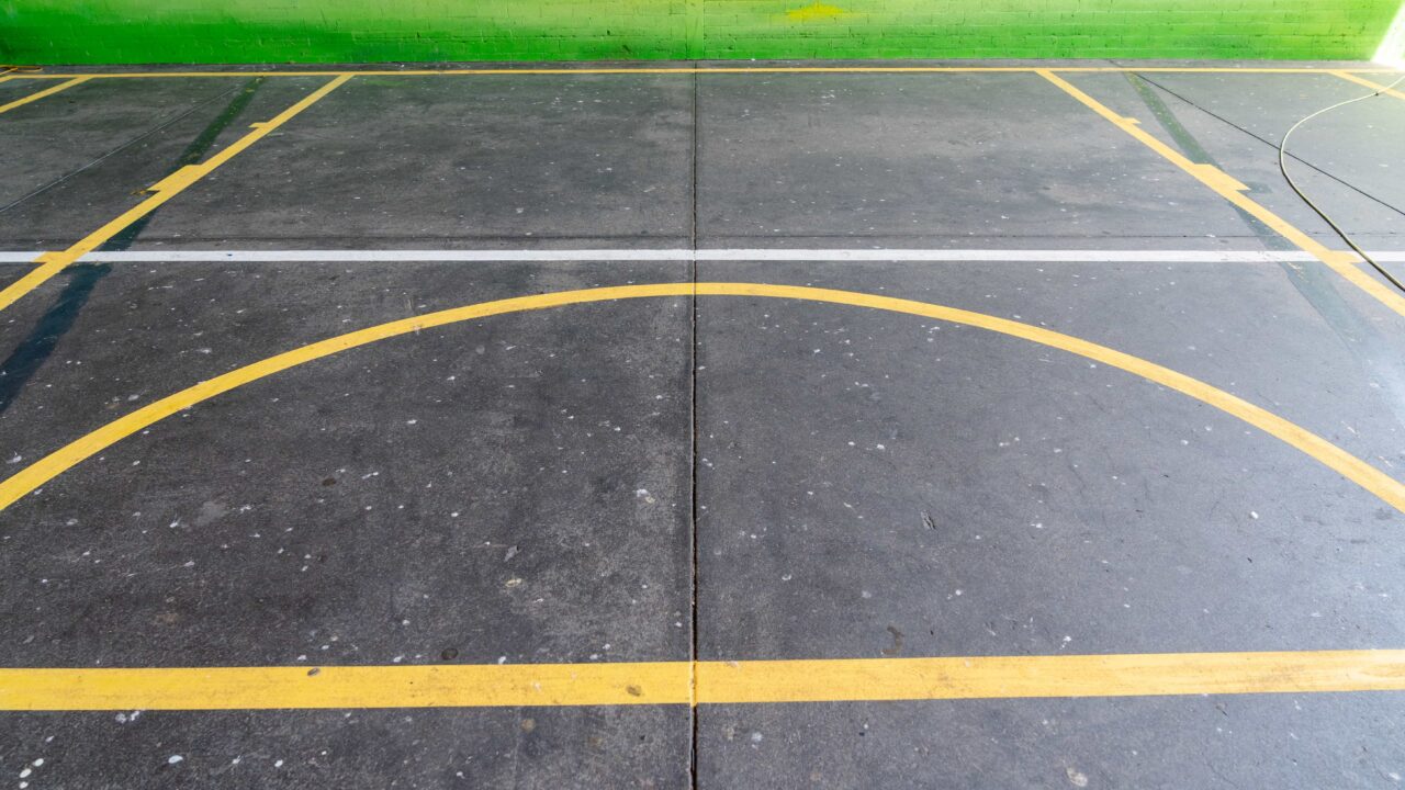 an outdoor sports court at springwood high school features meticulously crafted line marking, though the yellow lines have faded slightly against the vibrant green wall in the background.