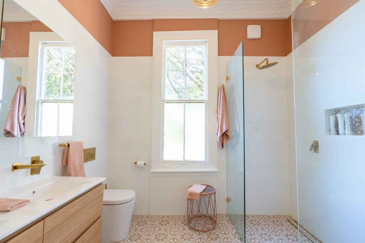 modern bathroom with a walk in shower, glass partition, patterned tile floor, window, vanity with sink, toilet, and rose gold accents. subtle interior painting enhances its elegance and highlights timeless trends in design.