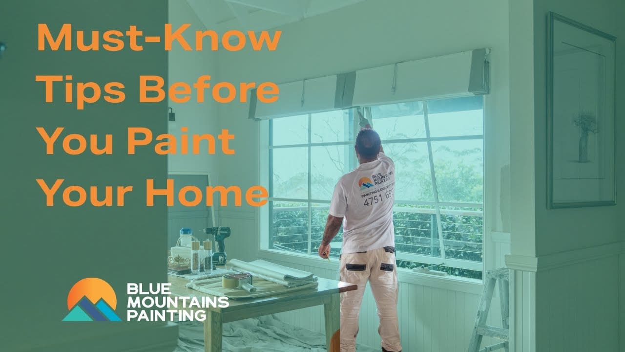 A painter stands by a large window preparing to paint your home; text reads "Must-Know Painting Tips Before You Paint Your Home" with a Blue Mountains Painting logo.